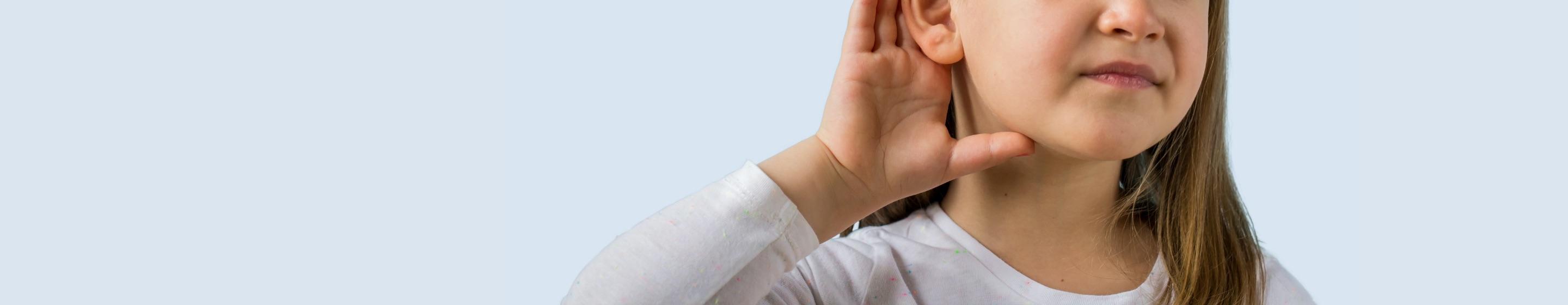 A young girl cups her hand around her ear.
