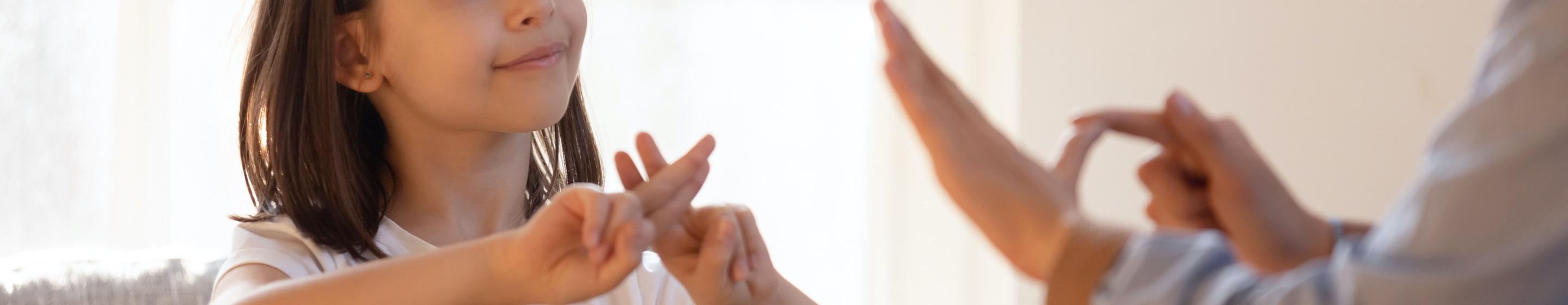 A young girl practices sign language with an adult.